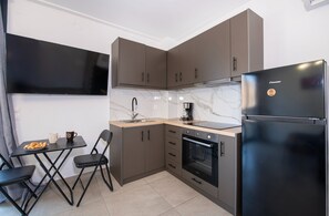 A compact kitchen with a built-in oven, a refrigerator, and a dining area with a table and chairs. - Halepa Apartment in Chania Esther 1 (Chania)