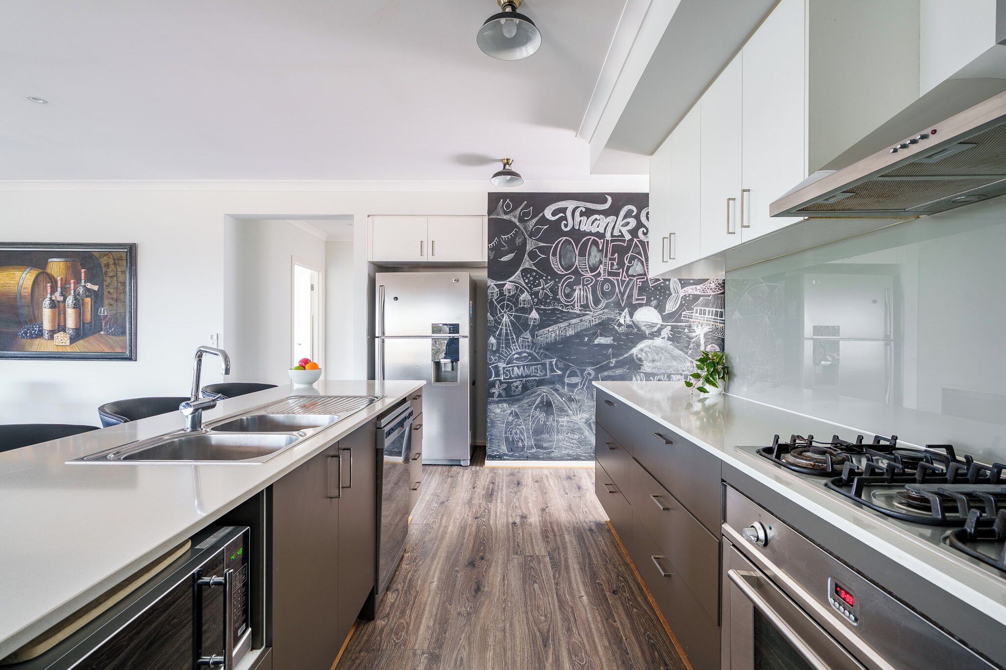Una cocina moderna con una isla central, electrodomésticos de acero inoxidable y una pared de pizarra con garabatos.