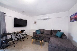Ein modernes Wohnzimmer mit einem grauen Sofa, einem schwarzen Couchtisch, einem an der Wand befestigten Fernseher und einem kleinen weißen Schrank.