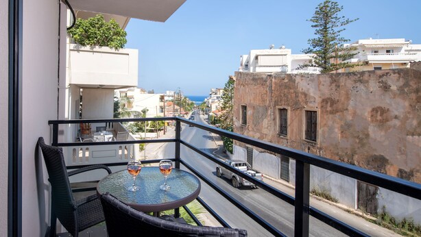 Ein Balkon mit Tisch und Stühlen, der auf eine Straße mit Gebäuden und einem klaren Himmel blickt.
