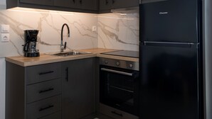 Uma cozinha moderna com armários escuros, uma geladeira preta, cafeteira e uma bancada de mármore.