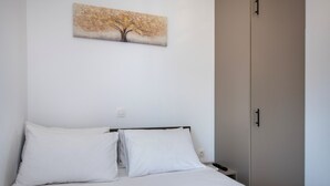 Quarto com cama, almofadas brancas, mesa de cabeceira, controle remoto e guarda-roupa.