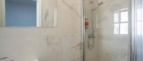 A bathroom with a glass-enclosed shower, a white sink, and a marble-tiled wall.