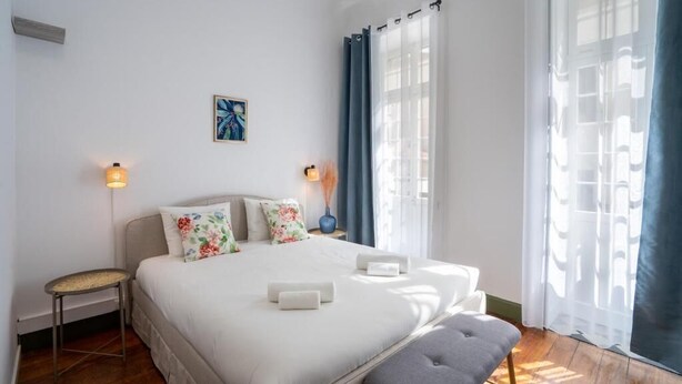A neatly arranged bedroom with a bed, bedside lamps, a small table, and a bench. - Zarco Suites by Sé Funchal (Funchal)