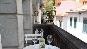 A balcony with a round table and two white chairs, a bottle of white wine, and a glass on the table. - Zarco Suites by Sé Funchal (Funchal)
