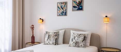A modern hotel room with a large bed, two wall-mounted lamps, and two framed artworks.