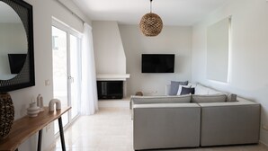 Un salon moderne avec un canapé d’angle, un téléviseur à écran plat fixé au mur, une cheminée et une grande fenêtre avec des rideaux.
