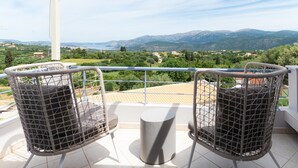 Un balcon agrémenté de deux fauteuils en osier et d’une petite table, offrant une vue panoramique sur un paysage magnifique, avec des montagnes et une végétation luxuriante.