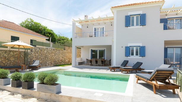 Une maison moderne à deux étages, dotée d’une piscine, d’un espace de détente extérieur et d’un mur en pierre.