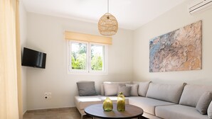 Een moderne woonkamer met een bank, een salontafel, een aan de muur bevestigde televisie en een groot raam met uitzicht op groen.