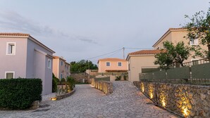 Une rue pavée, bordée de bâtiments : d’un côté, un mur de pierre, de l’autre, une clôture.