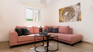 Un salon moderne avec un canapé d’angle rose, une table basse ronde et un grand tableau abstrait accroché au mur.