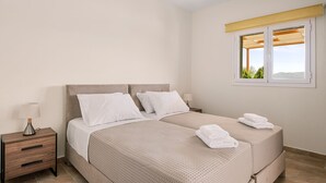 Une chambre avec deux lits, une table de chevet avec une lampe et une fenêtre donnant sur un paysage verdoyant.