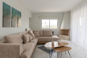 En moderne stue med en beige hjørnesofa, et rundt bord og et vindue med lette gardiner.