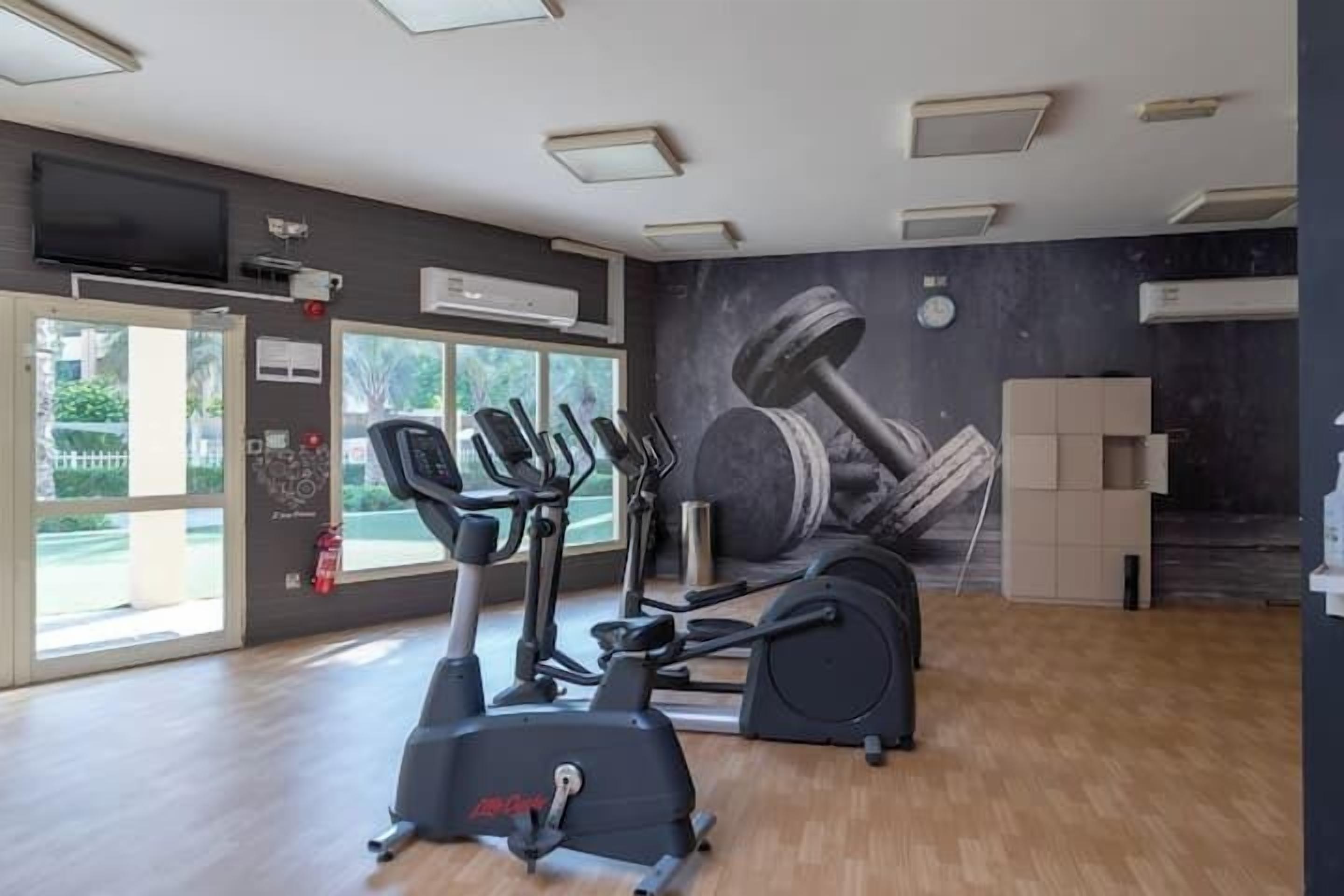 Un gimnasio con equipo de ejercicio, un ventanal grande y un mural de mancuernas.