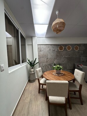 Een eetruimte met een ronde houten tafel, vier stoelen, een geweven hanglamp en een stenen muur met ronde decoraties.