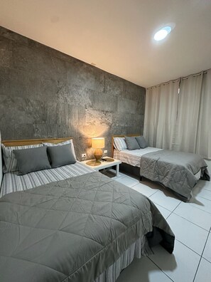 Een hotelkamer met twee bedden, een betonnen accentmuur, een nachtkastje met een lamp en een raam met gordijnen.