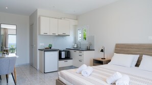 Een moderne hotelkamer met een bed, een kleine kitchenette, een zithoek en uitzicht op het omliggende landschap.