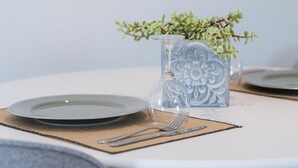 Een eettafel met een glazen vaas met een plant, een bord, bestek en een servet.