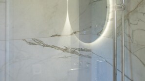 Een moderne badkamer met een marmeren wand, een handdouche en een ingebouwd ovaal spiegel.