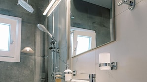 A modern bathroom with a large mirror, a vessel sink, a handheld showerhead, and a towel rack. - Standard Triple Room (Travliata)