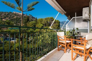 A balcony with a view of a mountainous landscape, wooden furniture, and a table with wine glasses.