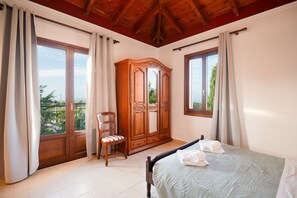 Ein Schlafzimmer mit einem Bett, einem Holzschrank, einem Sessel und einem Balkon mit Vorhängen.
