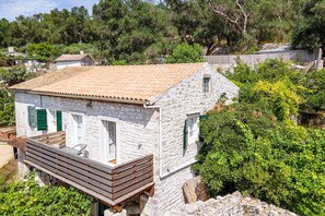 Une maison en pierre avec un toit en tuiles, une terrasse en bois et des volets verts.