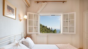 Un dormitorio con una cama grande, una ventana con contraventanas abiertas, una lámpara de noche y un cuadro enmarcado en la pared.