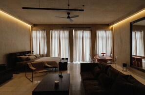 Quarto de hotel moderno com cama, sofá, mesa de centro e área de jantar com mesa e cadeiras.