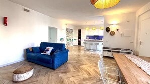 A modern living room with a blue sofa, a wooden dining table, and a kitchen in the background. - Apartment in a semi-detached house with independent entrance.-Rif. Casa Nina (San Vincenzo)