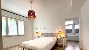 A hotel room with a large bed, a hanging light fixture, a nightstand with a lamp, and a view of the bathroom. - Apartment in a semi-detached house with independent entrance.-Rif. Casa Nina (San Vincenzo)