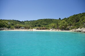 A coastal area with clear turquoise waters, a sandy beach, and a forested hillside. - Thodoroulis in Paxi with 1 bedrooms and 1 bathrooms (Paxi)
