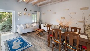 Ein gemütliches Wohnzimmer mit einer Couch, einem Esstisch und Stühlen. Ein Fenster bietet Blick auf eine grüne Umgebung.
