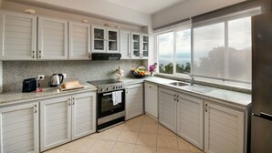Eine moderne Küche mit weißen Schränken, einem Edelstahlkühlschrank, einem eingebauten Ofen und einem großen Fenster mit Meerblick.