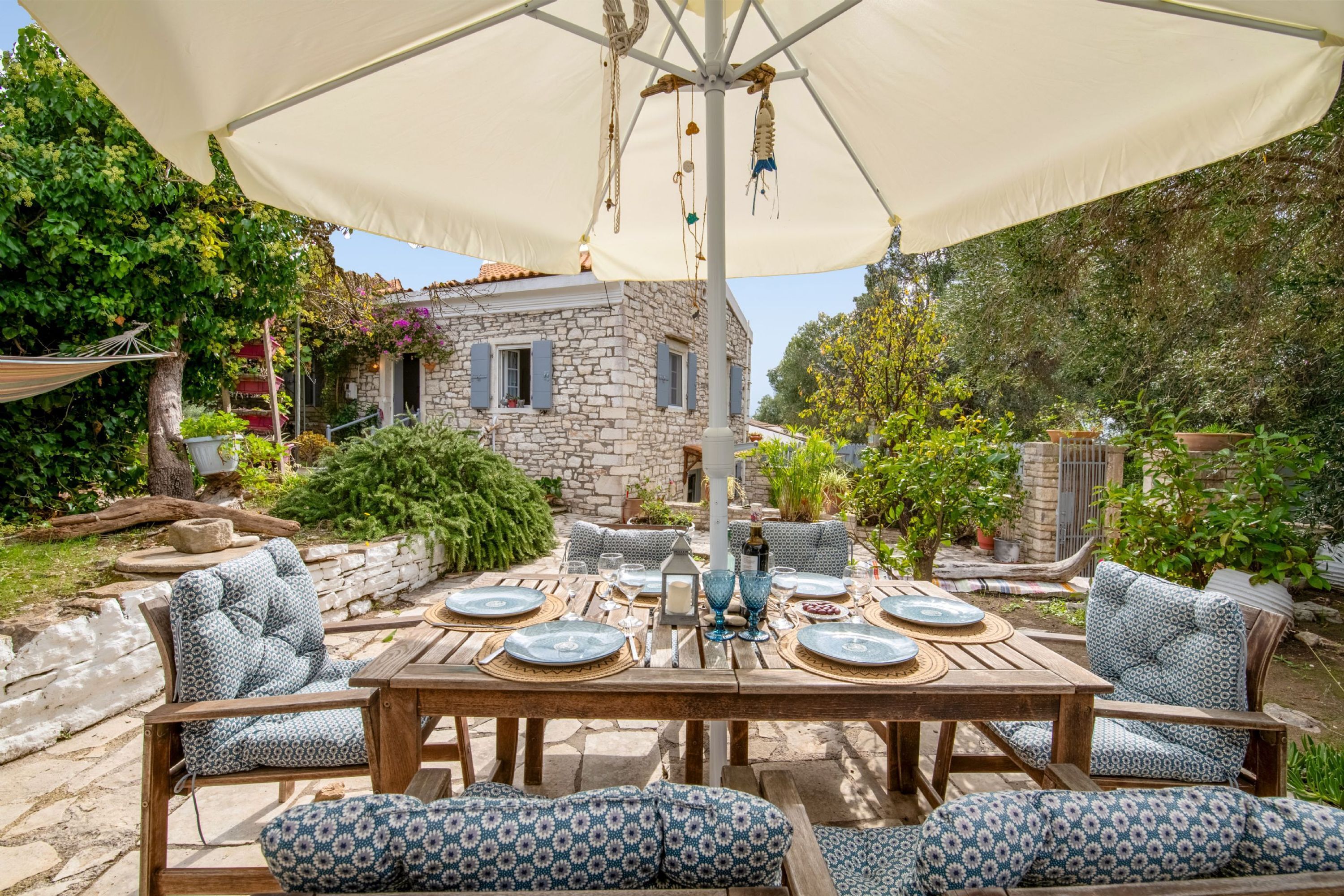 An outdoor dining area with a stone building in the background, surrounded by greenery.