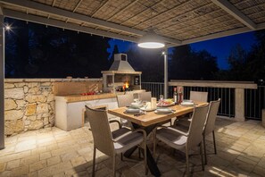 Eine Außenpatio mit einer Steinmauer, einem Backofen aus Ziegeln und einem Esstisch für vier Personen.