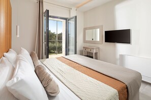 Ein Hotelzimmer mit Bett, Fernseher, kleinem Schreibtisch und Balkon mit Blick.