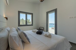 A bedroom with a bed, pillows, towels, a window, and a door leading to a balcony. - Areti-Elena Oxomeria (Paxi)