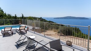 Ein Poolbereich mit Liegestühlen und einem Tisch, mit Blick auf einen Strand und das Meer.