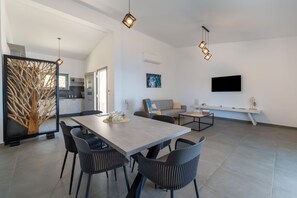 A modern living room with a dining area, a kitchen in the background, and a TV mounted on the wall. - Aphitriti Oxomeria in Paxi (Paxi)