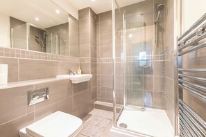 A modern bathroom with a glass-enclosed shower, a white toilet, and a vanity with a mirror and sink. - Stylish Flat in Romford - 5mins for Elizabeth Line (Romford)