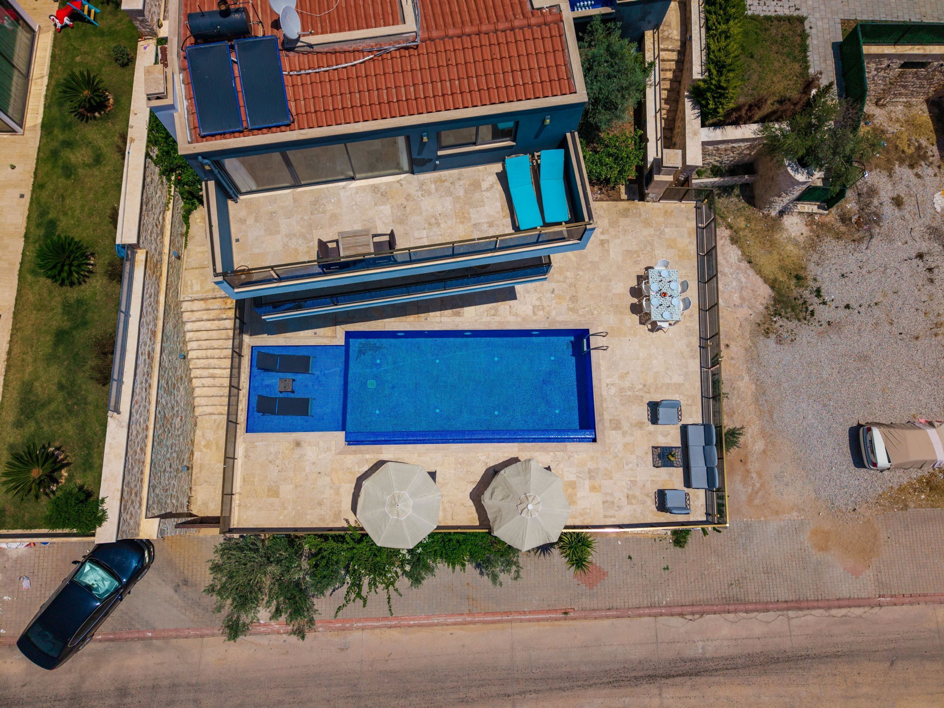 Una casa moderna con piscina, mobiliario exterior y un coche aparcado cerca.