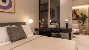 Een moderne hotelkamer met een bed, een bureau, een stoel, een bijzettafeltje, een potplant en kunst aan de muren.