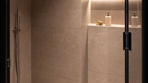 Une salle de bain moderne dotée d’une douche à l’italienne, d’une porte en verre et d’une étagère pour les articles de toilette.