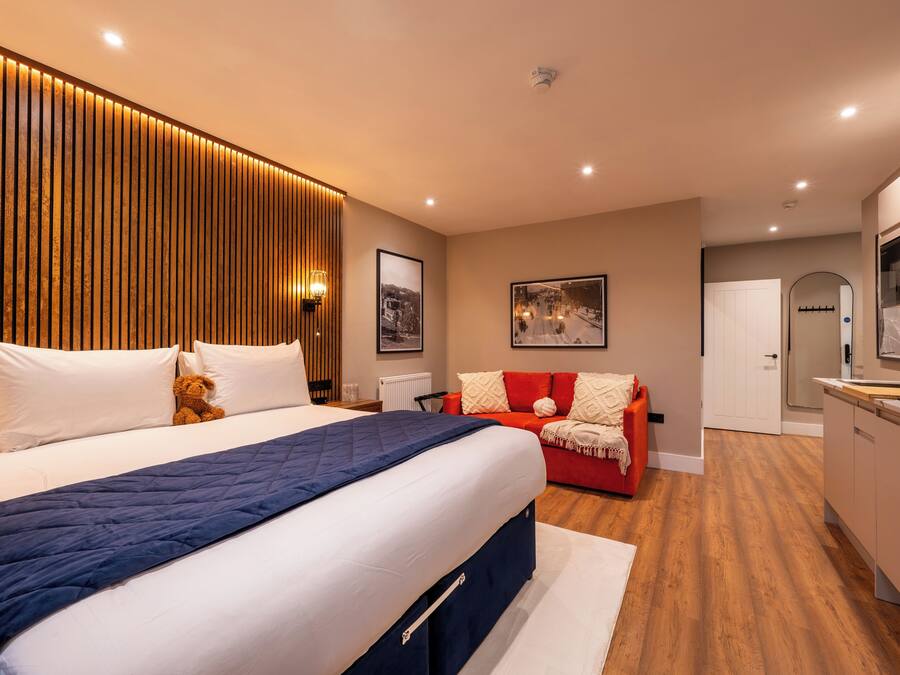 Una habitación de hotel moderna con una cama grande, un sofá rojo, una zona de cocina y un revestimiento de pared de madera.