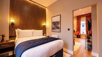A modern bedroom with a large bed, a wooden panel wall, a framed picture, and a view into a dining area.