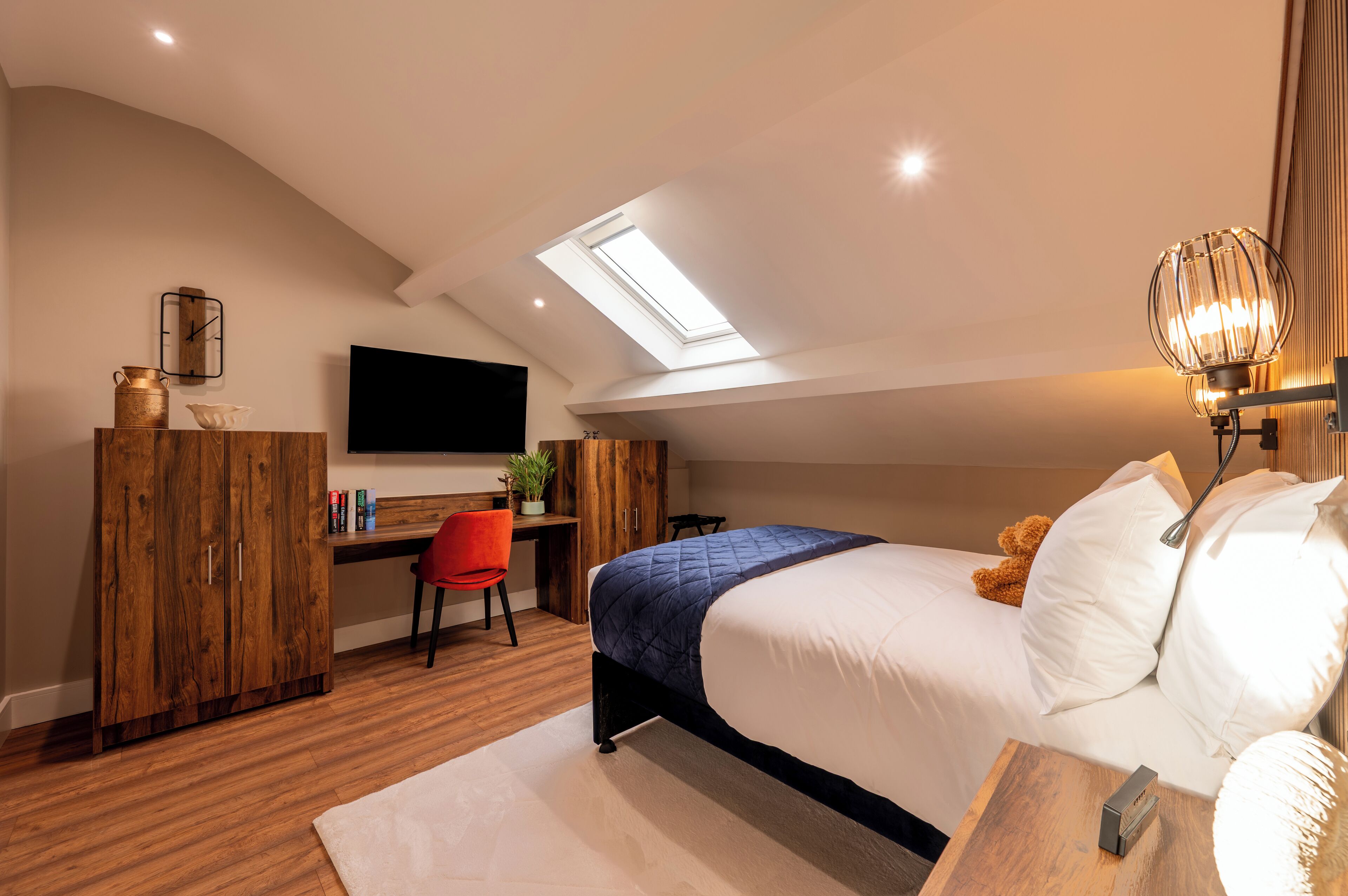 A bedroom with a skylight, a bed, a desk, and a chair.
