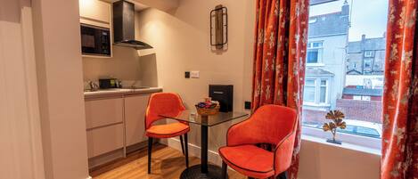 Una cocina compacta con electrodomésticos modernos, un comedor con dos sillas y una ventana con cortinas.