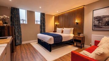 Un dormitorio moderno con cama, mesitas de noche, un sofá rojo, suelo de madera y una ventana con cortinas.